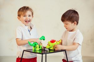 Two boys playing with toy dinosaurs at a table