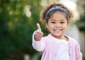 Smiling girl giving a thumbs-up outdoors