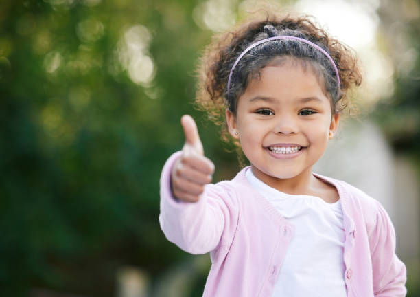 Smiling girl giving a thumbs-up outdoors
