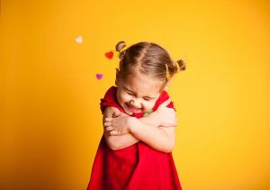 Little girl in a red dress hugging herself against a yellow background