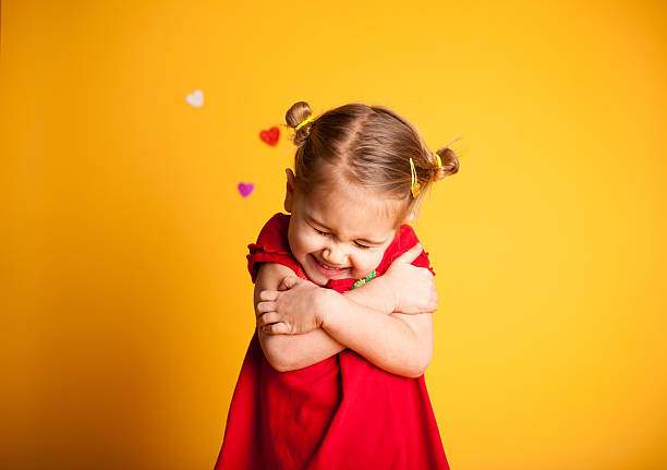 Little girl in a red dress hugging herself against a yellow background