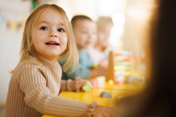 Young girl smiling at a classroom table with other children