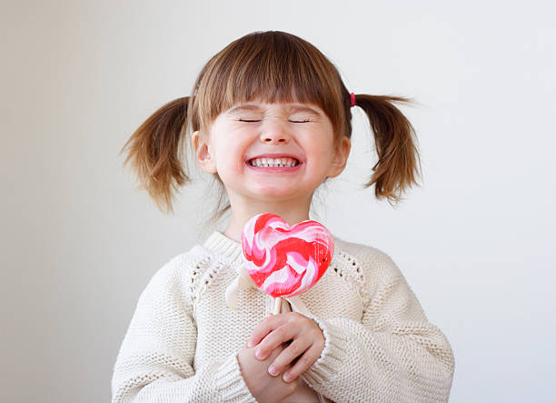 Smiling girl with pigtails holding a heart-shaped lollipop